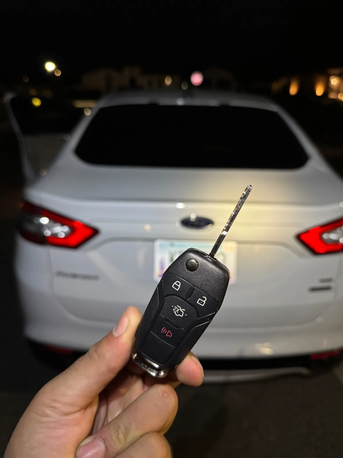 Replacement Ford flip key held behind a Ford Fusion at night during a real mobile locksmith service call