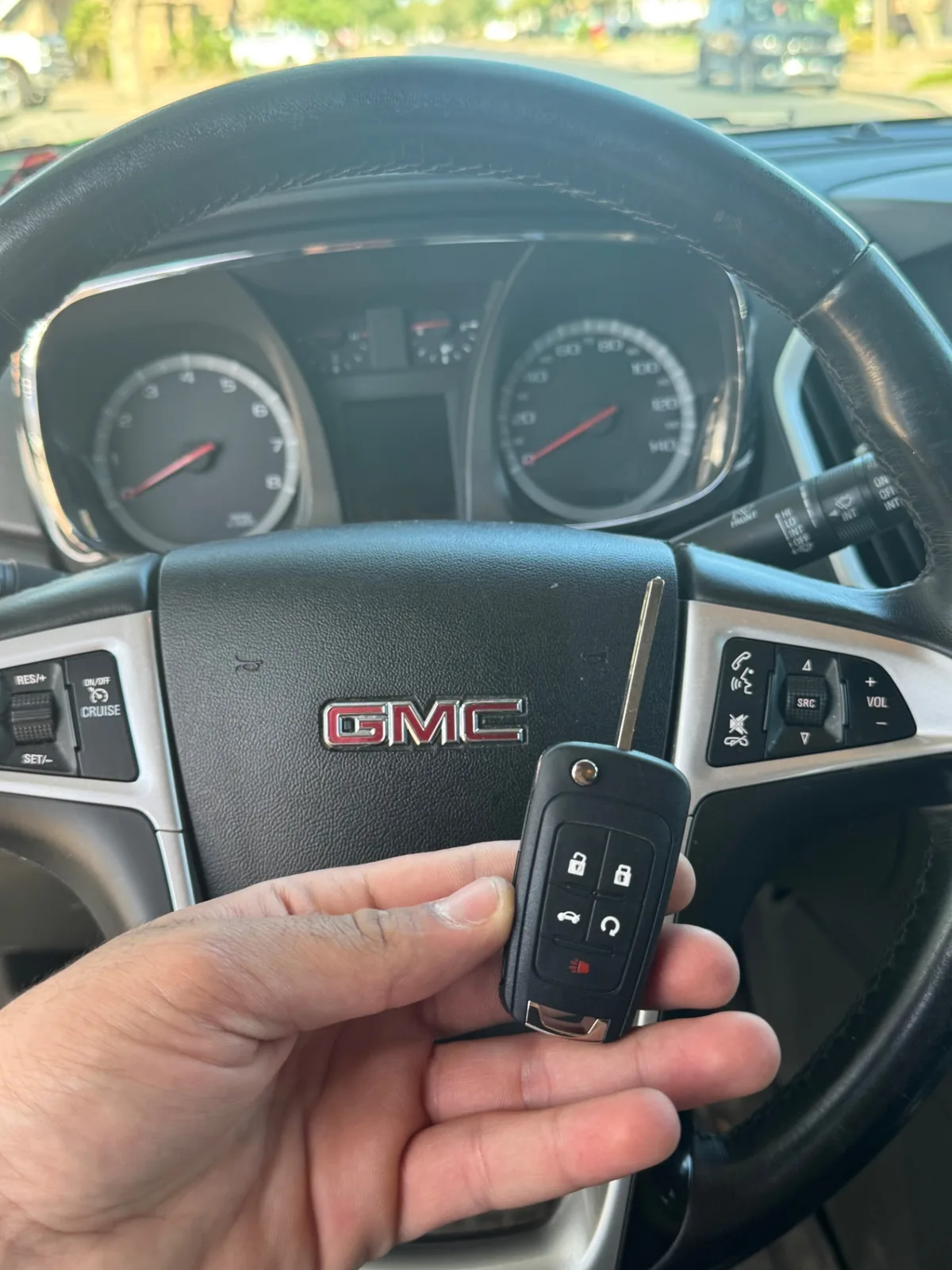 New GMC remote key held in front of a GMC steering wheel after a completed locksmith job